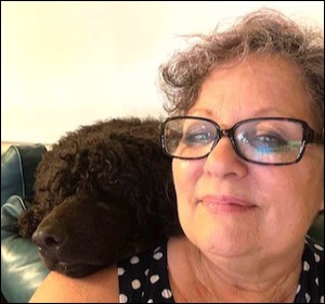 Woman smiling with black poodle head on shoulder
